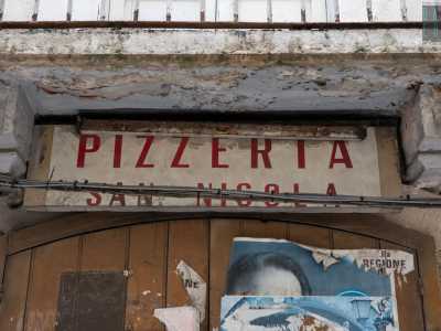 L�insegna � disposta su un vecchio portone in legno marrone sul quale sono stati attaccati negli anni numerosi volantini pubblicitari. � evidente lo stato di abbandono del posto che � stato attivo dal 1980 al 1990
